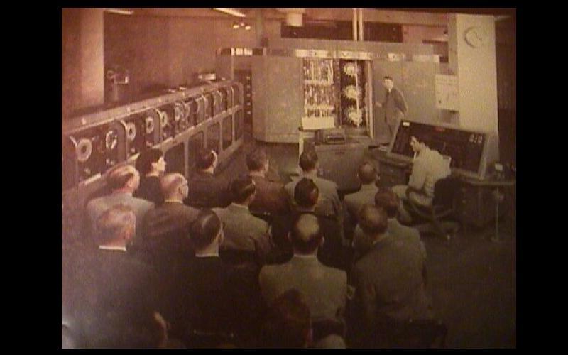 保罗Chinitz & 图为保罗·奇尼茨在雷明顿-兰德公司纽约计算中心打开UNIVAC 1中央处理器的门, 公司. 听众是编程课程中的一类客户. 电脑操作员是弗兰克·萨斯，他是高级教官之一. 珍·詹宁斯·巴蒂克在雷明顿-兰德公司工作期间曾与两人密切合作. (原始照片由保罗Chinitz捐赠给Jean JENNINGS Bartik计算机博物馆.)