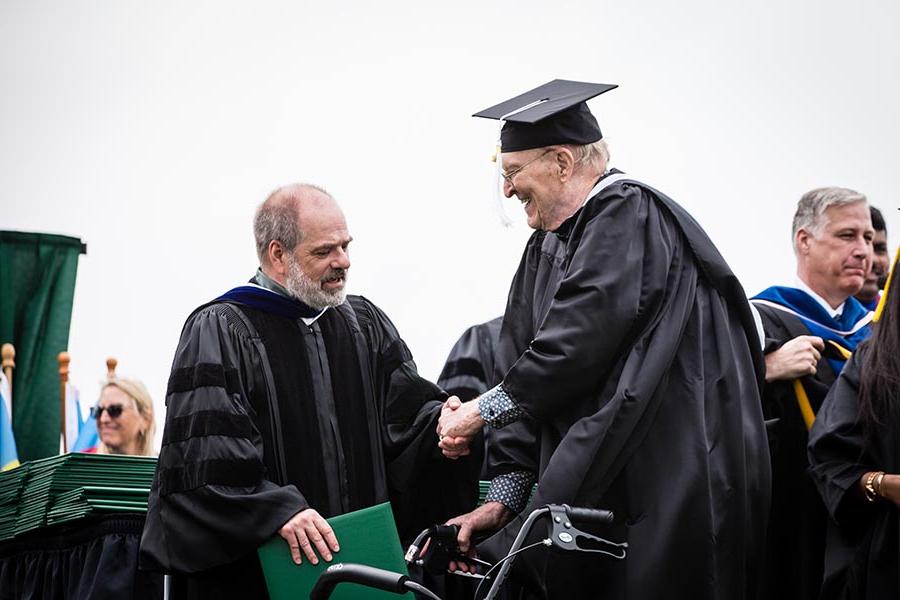 Dr. 迈克·施泰纳, associate provost of undergraduate studies and dean of the College of Arts and Sciences, congratulated 戈登 Hill as he crossed the commencement stage at Bearcat Stadium. 